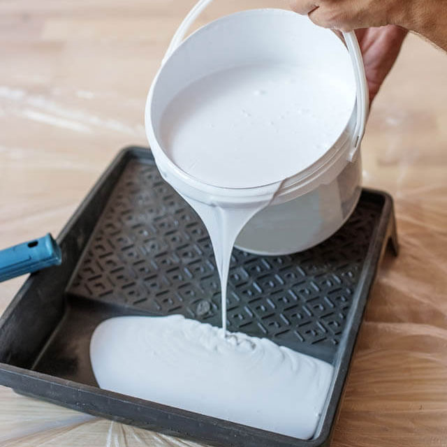 pouring white interior paint into a paint tray
